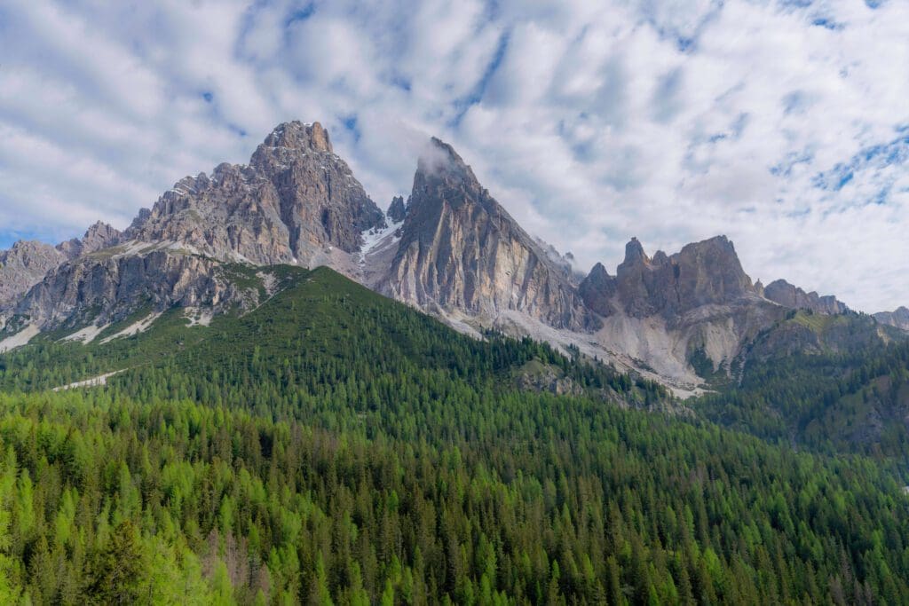 Unbeleavable view of the Dolomite mountains towering into the clouds with a dense forest at the base