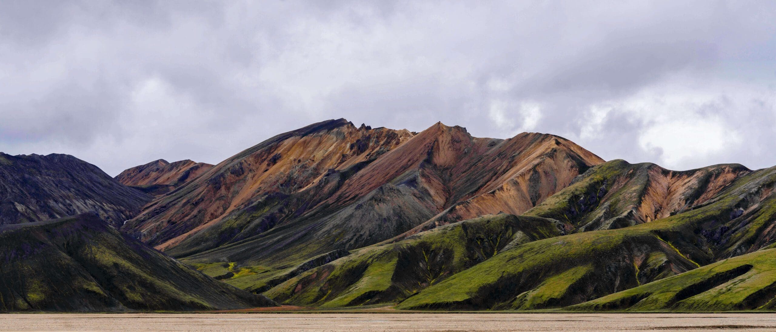 Large jagged brownish-red mountains mixed with the rolling green hills of the breathtaking Landmannalaugar