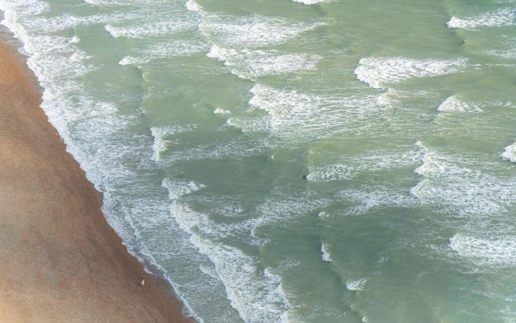 In the i360 high above the waves of the English Channel crashing against the beach as one woman walks alongside the water, one of the best things to do in Brighton