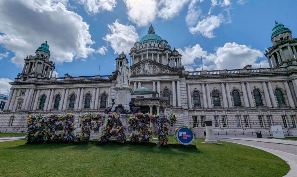 The clean white and teal historic city hall featuring a sculpture spelling "Belfast" made of flowers