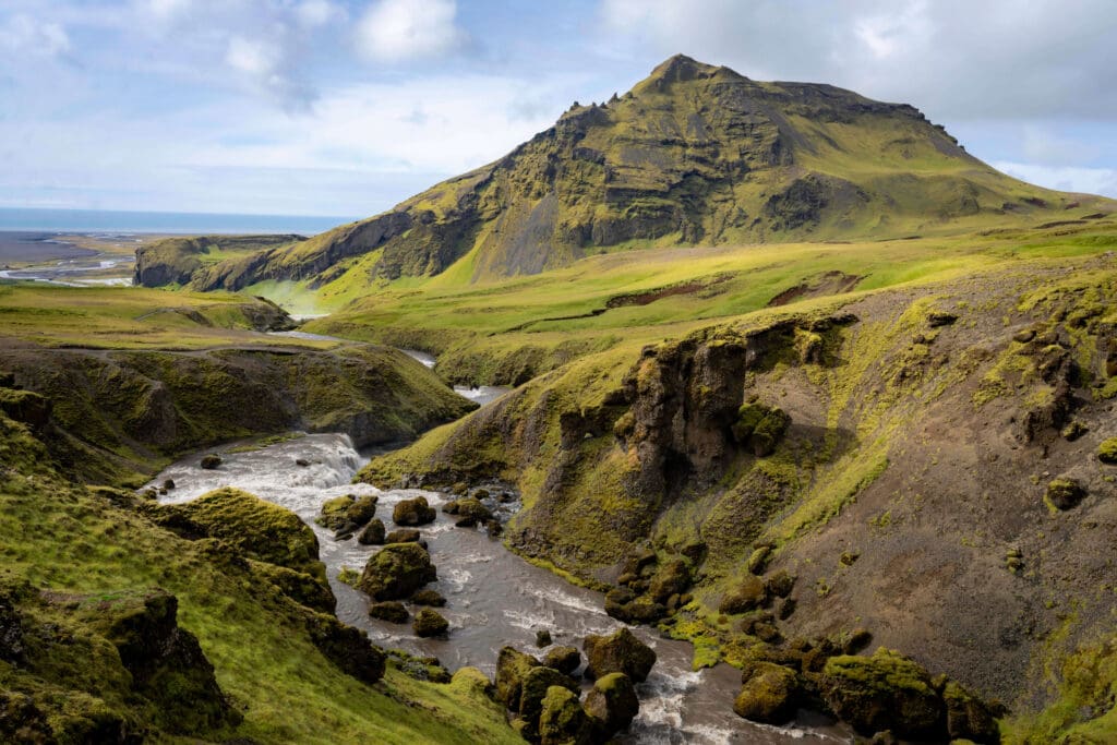 Hiking along a river running through the mountainous grassy Iceland landscape