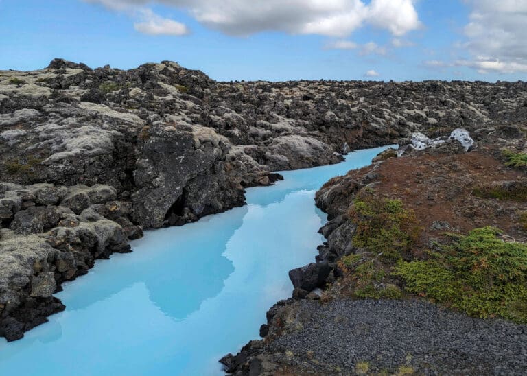 Glassy sky blue water of the Blue Lagoon Hotspring cuts through the volcanic rock