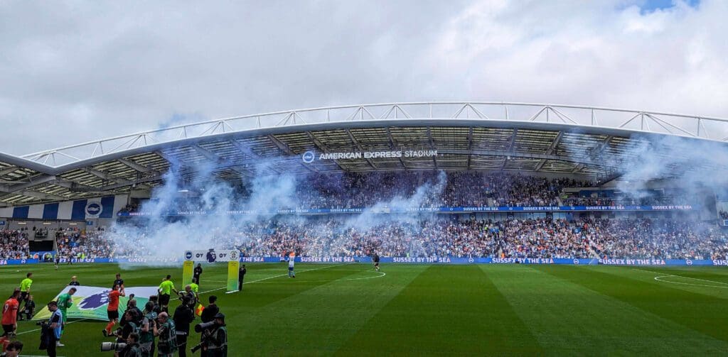 Blue flares spread smoke across the American Express Stadium as Brighton & Hove Albion FC take the pitch to play football