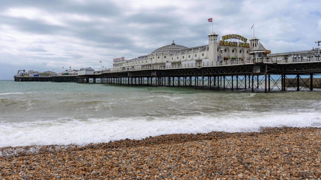 Calm waves rolling onto the shore underneath the long Brighton Palace Pier full of rides and shops