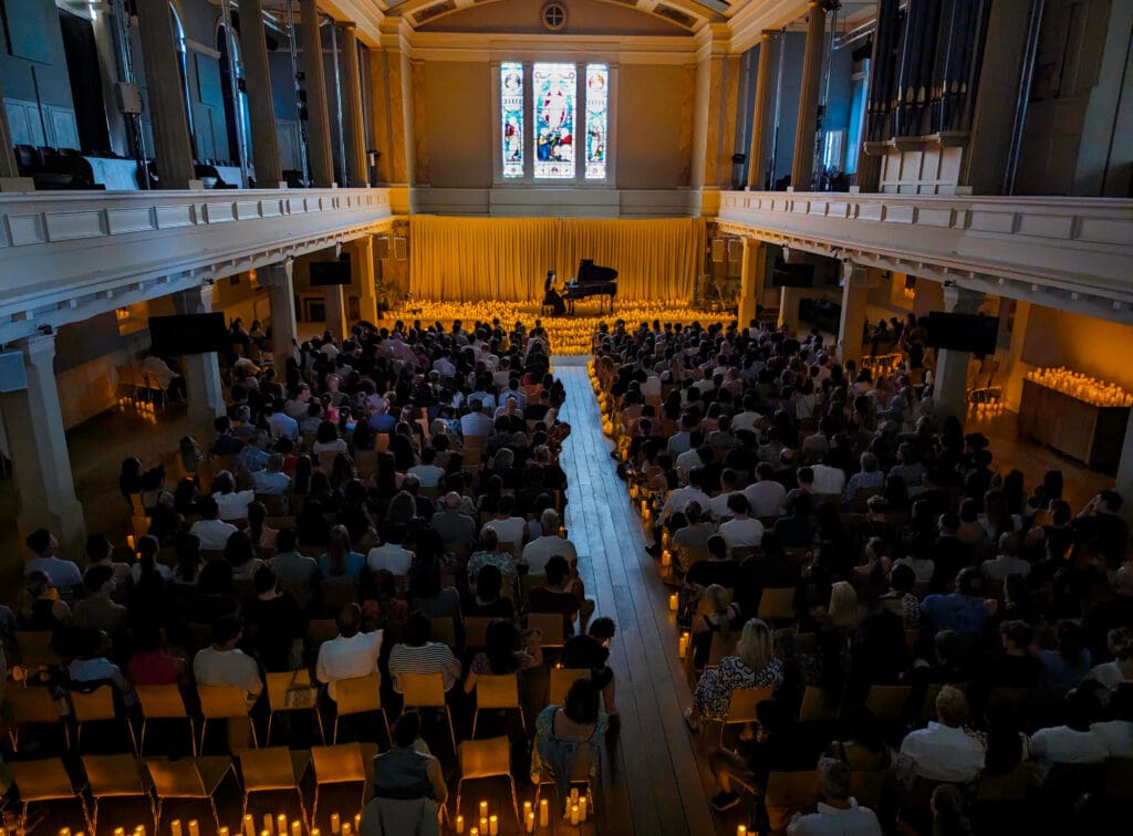 Hundreds of candles create an enchanting atmosphere as a lone pianist plays a piano on stage