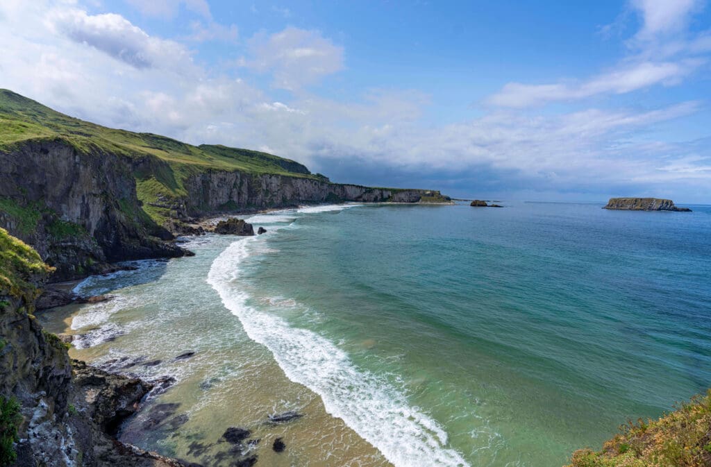 White cliffs tower above the ocean waves looking from Carrick A Rede Rope Bridge, one of the best things to do in Northern Ireland.