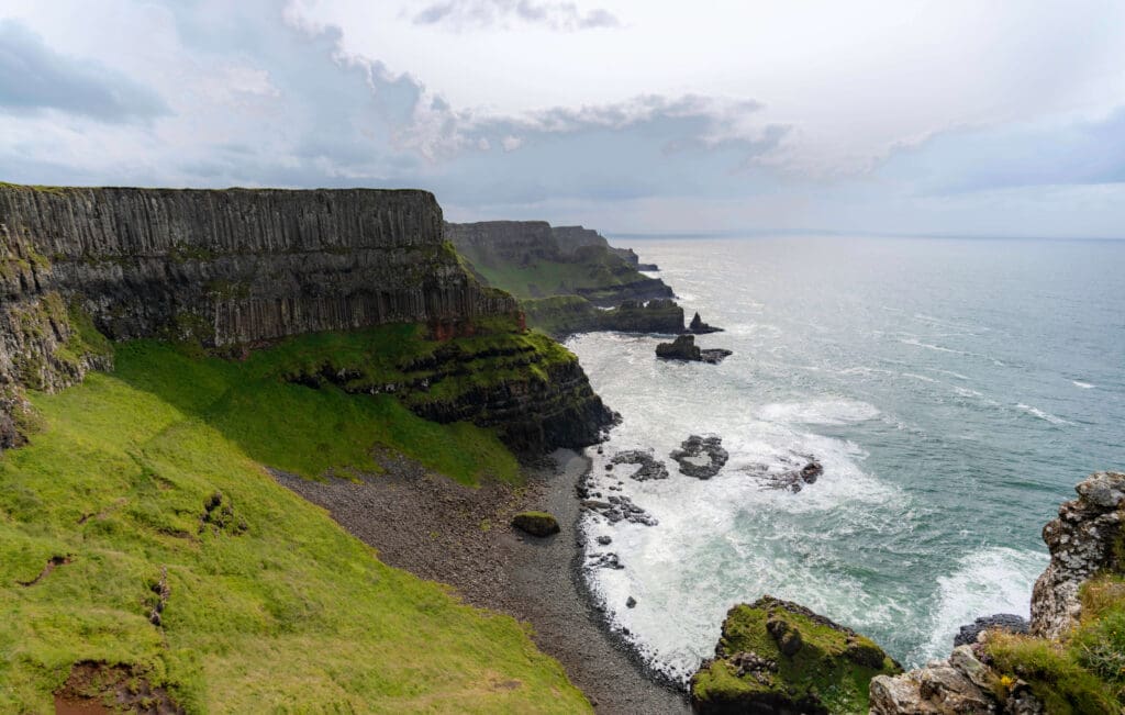 Green plateau cliffs overlooking the ocean as waves crash below while hiking the Causeway Coastal Route