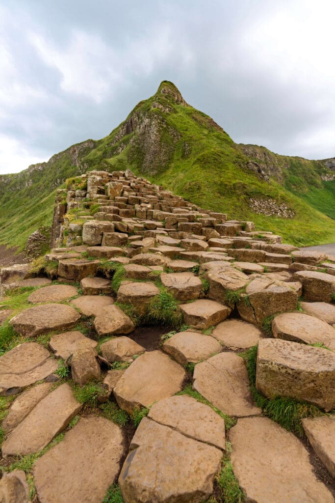 A smooth stone hexagon path leads up a hill with a large grassy mountain at Giant's Causeway, one of the best things to do in Northern Ireland.