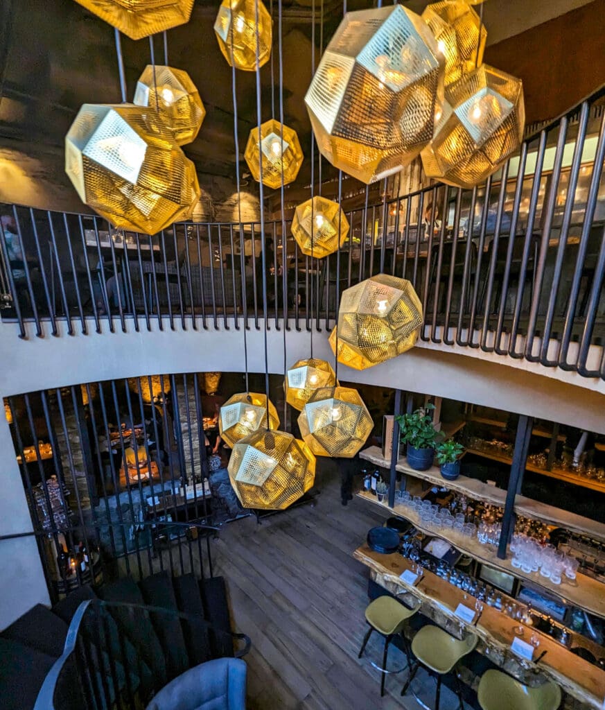 Yellow sphere chandelier lights hang down as you descend a spiral staircase to the lower bar of Grill Market Iceland