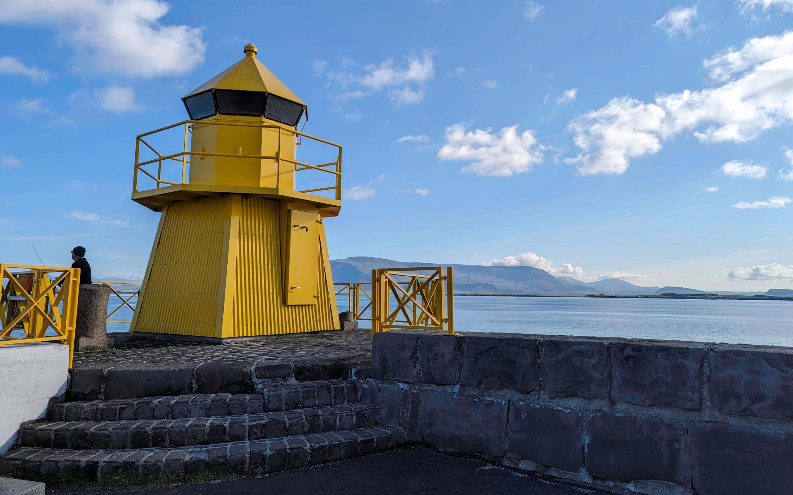 The bright yellow Ingolfsgardur Lighthouse overlooking the open ocean bay and bright blue sky