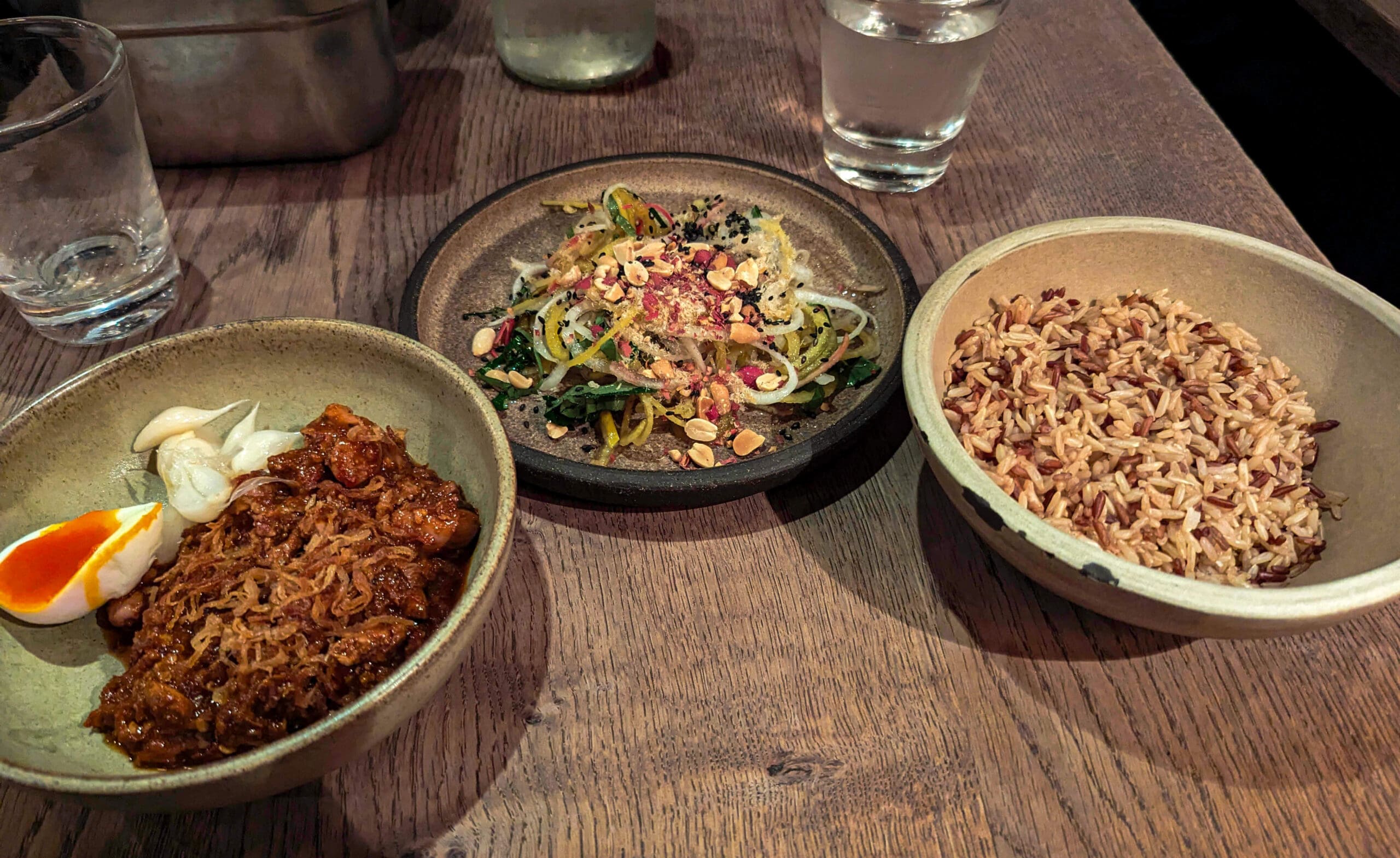 Three plates of rice, southern chicken livers, and seasoned mixed vegetables served in clay dishware from Kiln Soho