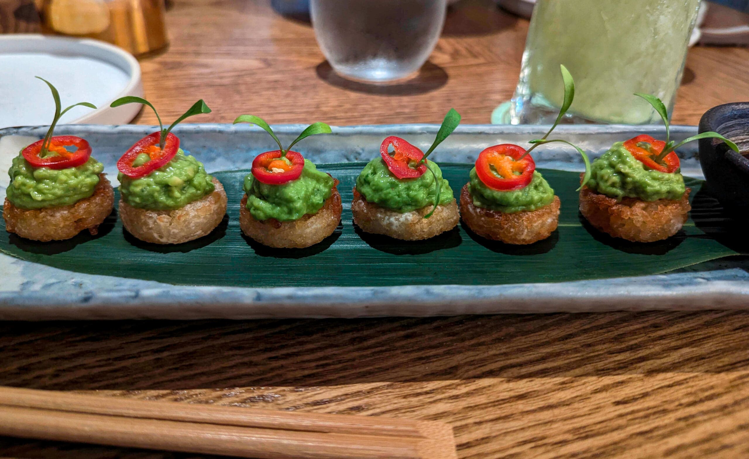 A plate lined with six crunchy rice balls topped with avocado, a red pepper slice and garnish ordered from Koyn restaurant