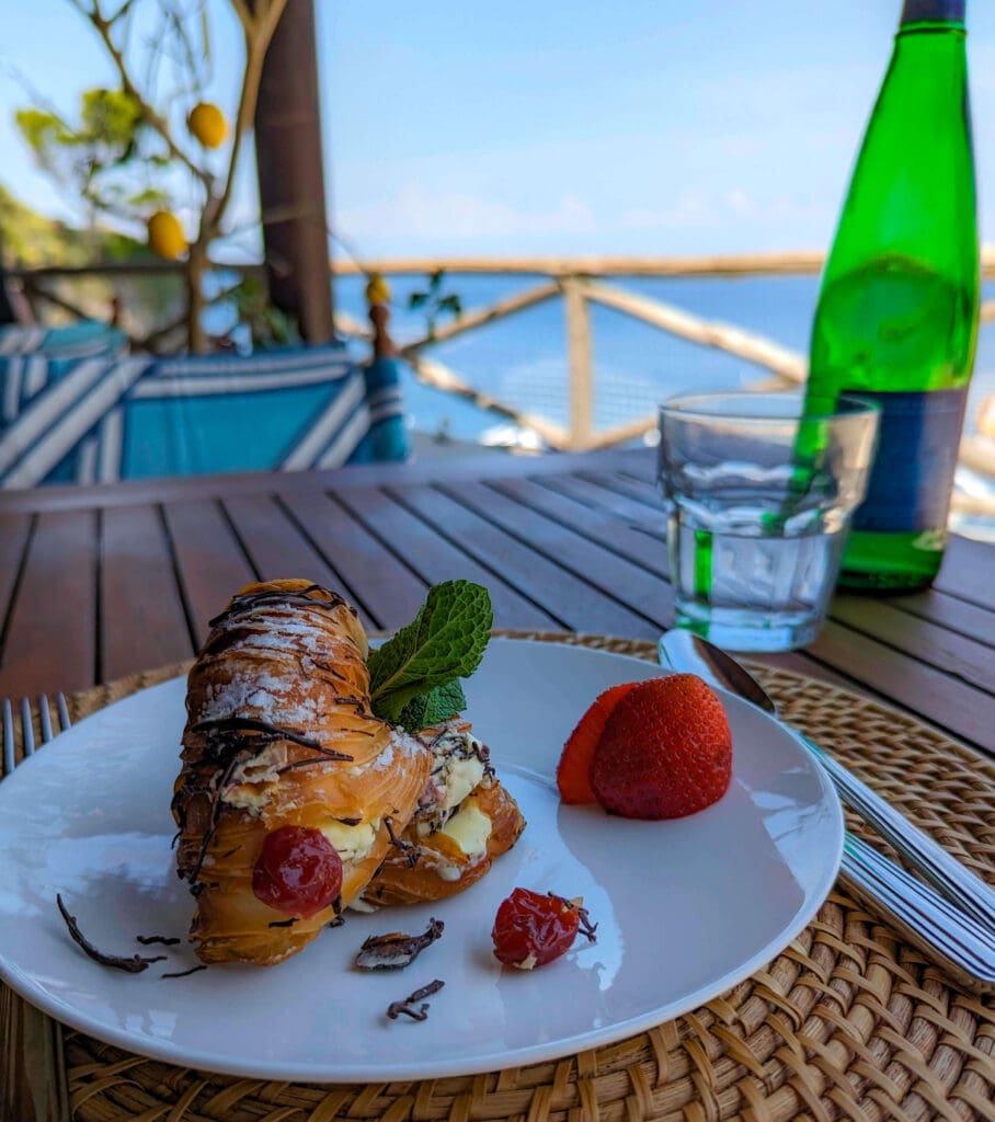 A flaky pastry filled with custard topped with chocolate drizzle and fresh fruit overlooking the ocean at La Baia Ristorante 