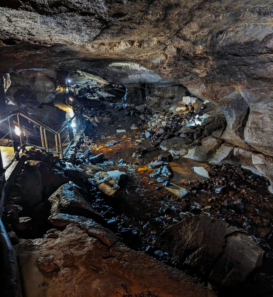 A lit concrete path runs along the cave wall following a slow river descending deeper into the Marble Arch Caves