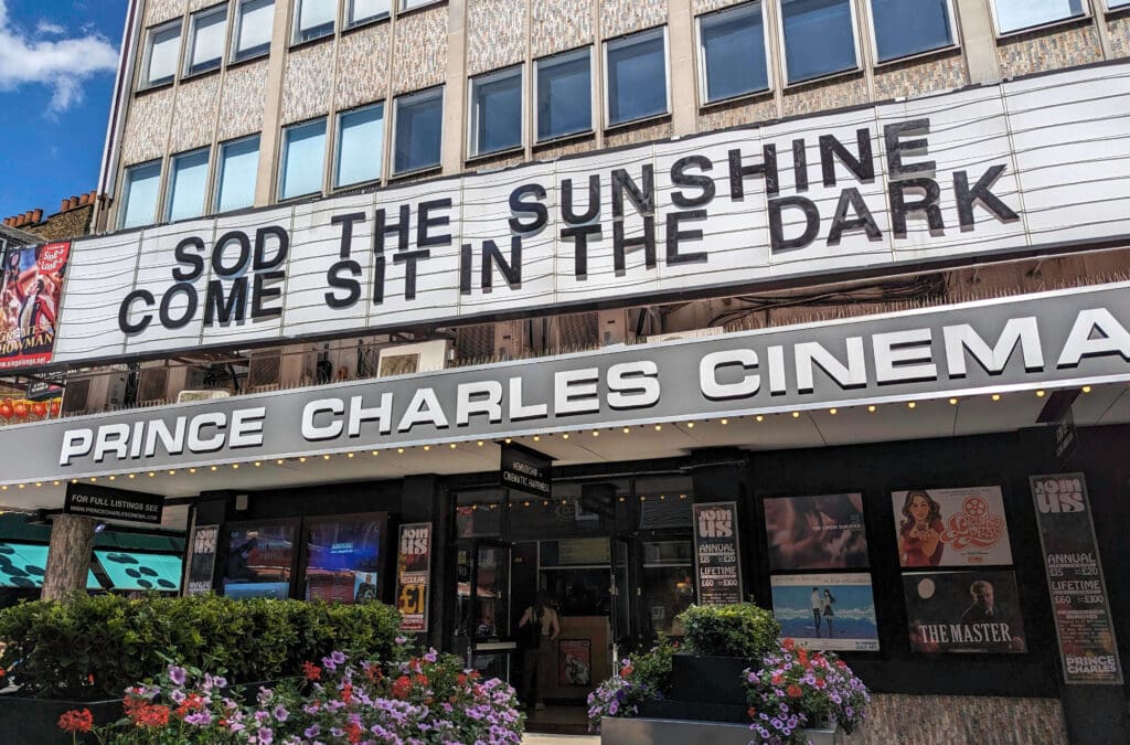 The outside sign of the Prince Charles Cinema in Soho that says "Sod the sunshine come sit in the dark"