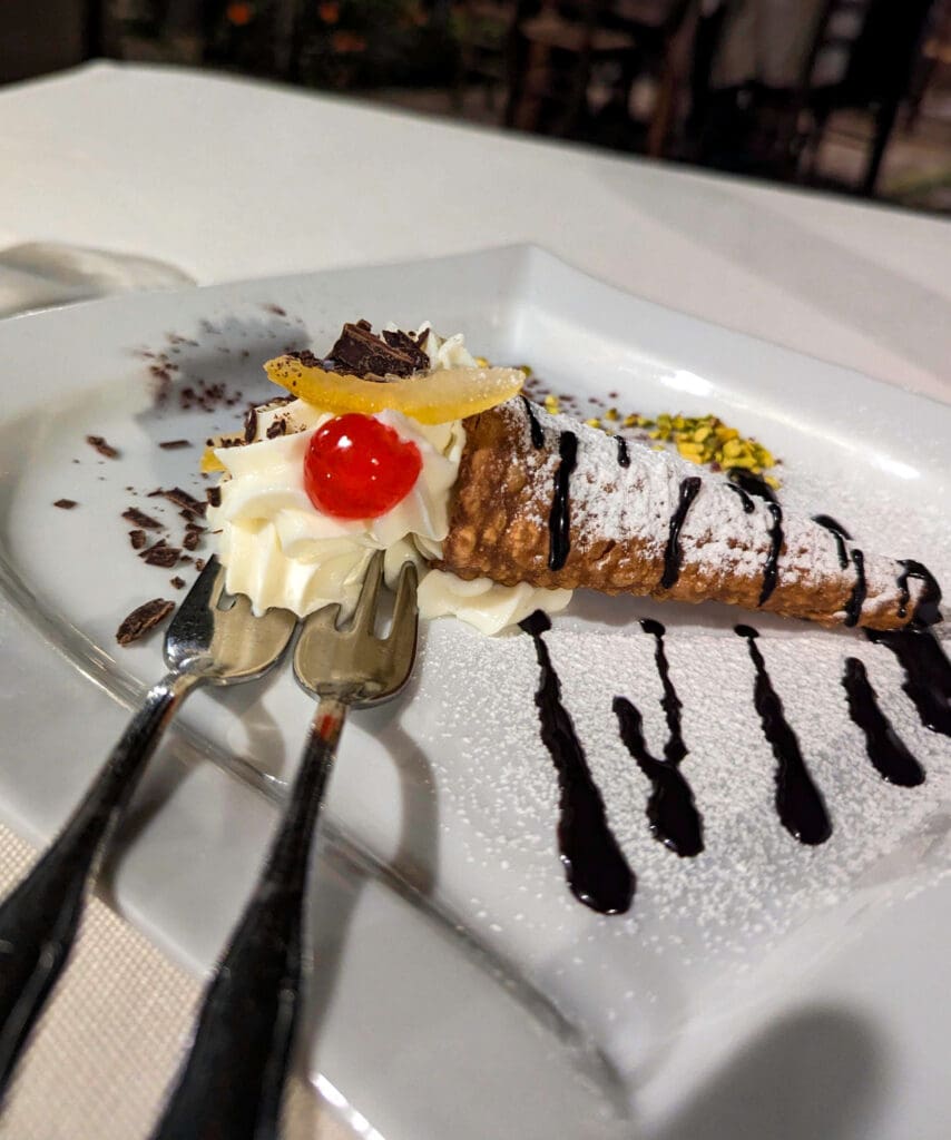 A cannoli stuffed with creamy custard and chocolate drizzle and a cherry on top served at Ristorante La Pergola in Procida