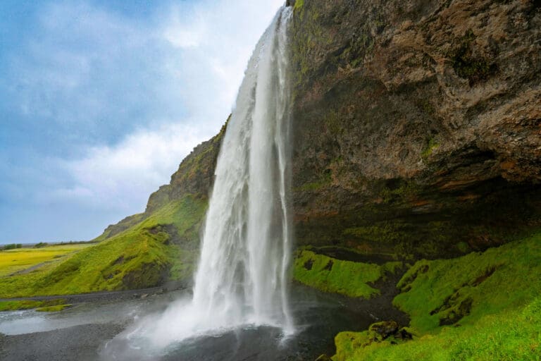 The Seljalandsfoss waterfall flowing off the overhang to the surrounding green ground below