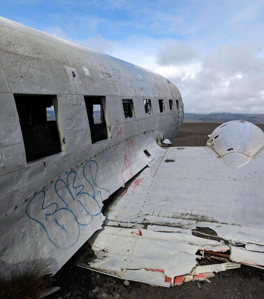 Silver hollowed remains of the Sólheimasandur Plane Wreck with some light graffiti surrounded by open Icelandic landscape