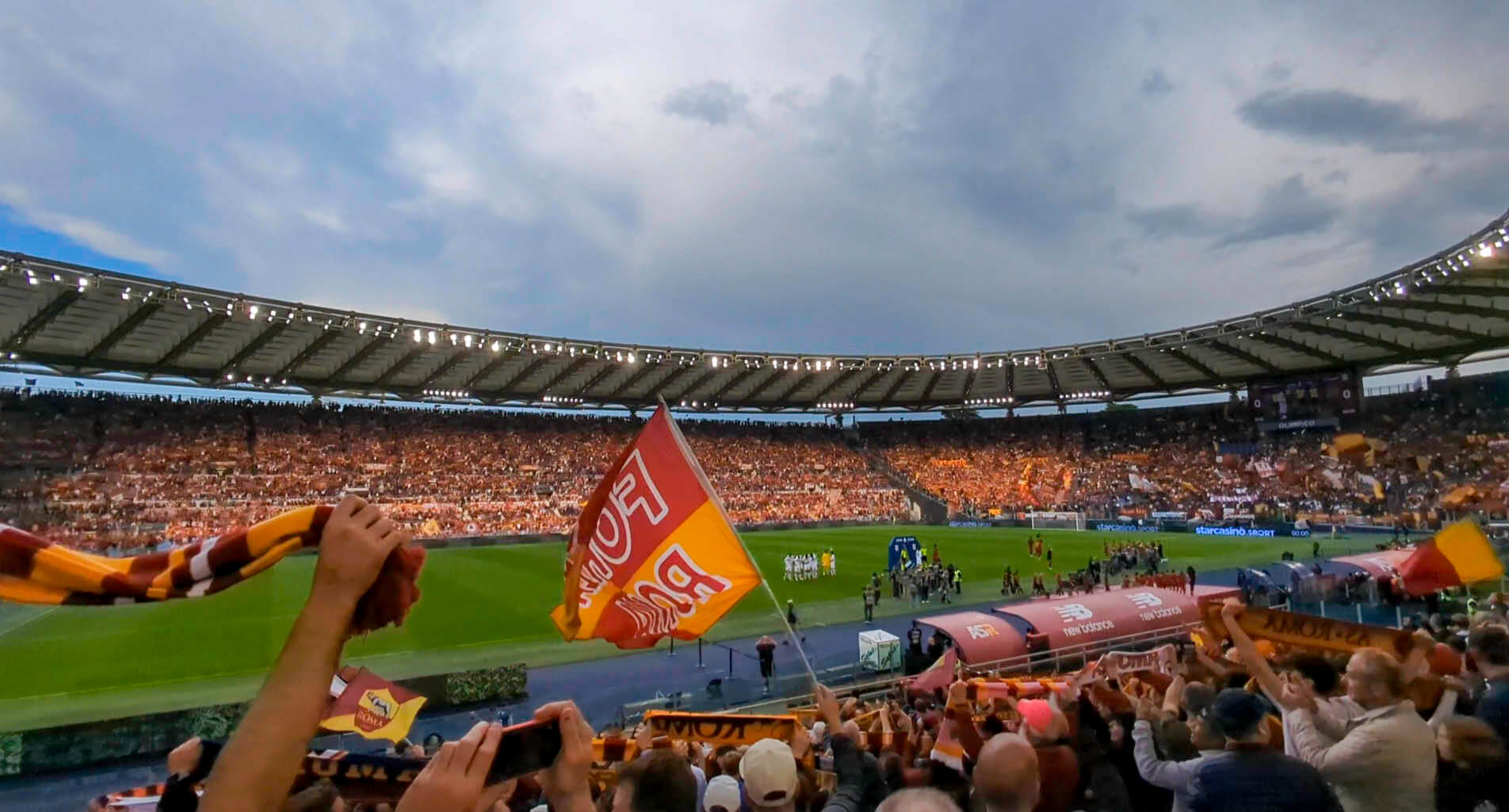 A roaring crowd chants and wave flags as they prepare for the Roma fc to take the pitch at Stadio Olimpico