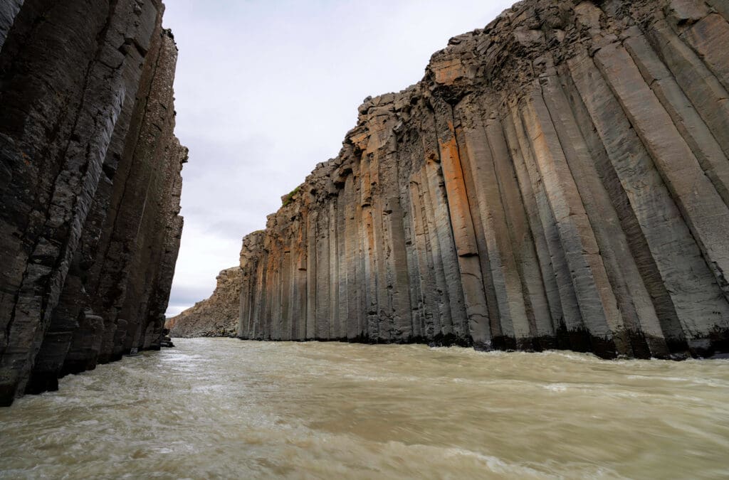 Water rushes through the tall rust-colored basalt columns of the Studlagil Canyon