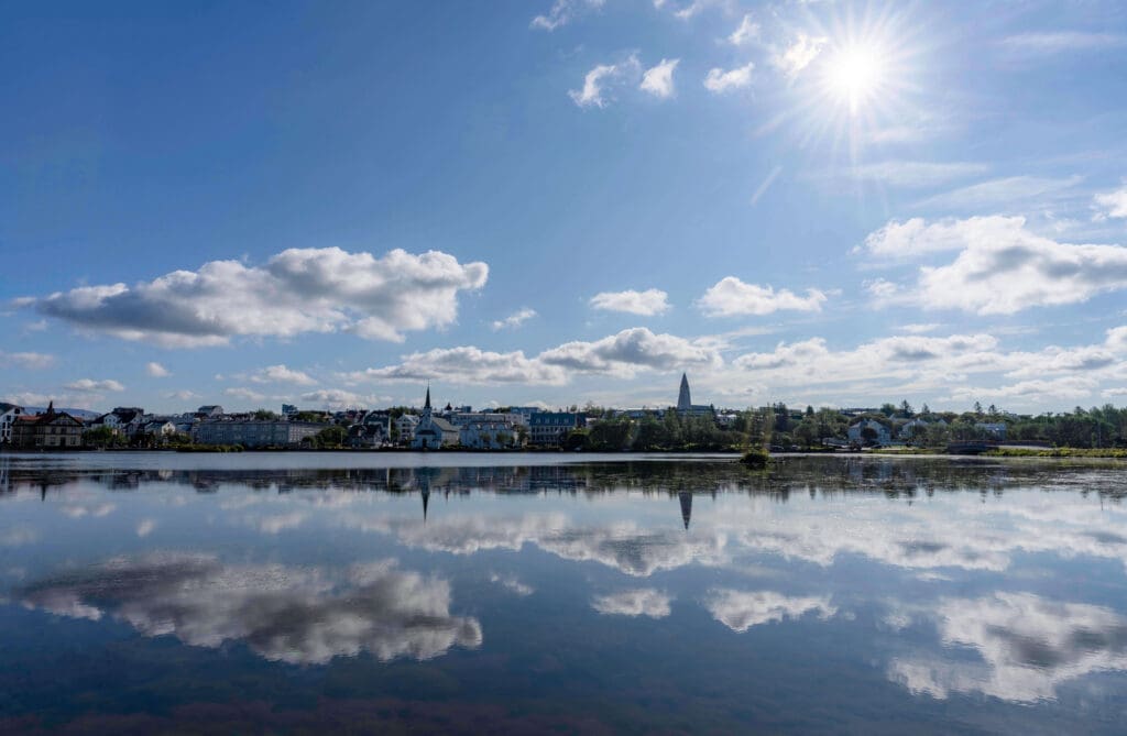 Sunny blue skies reflect off the smooth Tjornin Pond with Reykjavik city in the background