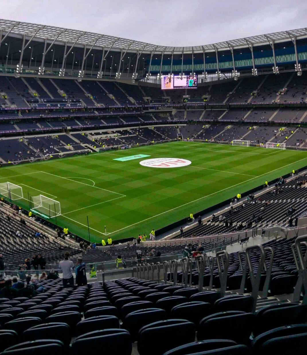 The green immaculate pitch and massive stadium of Tottenham Hotspur Stadium as people begin to find their seats