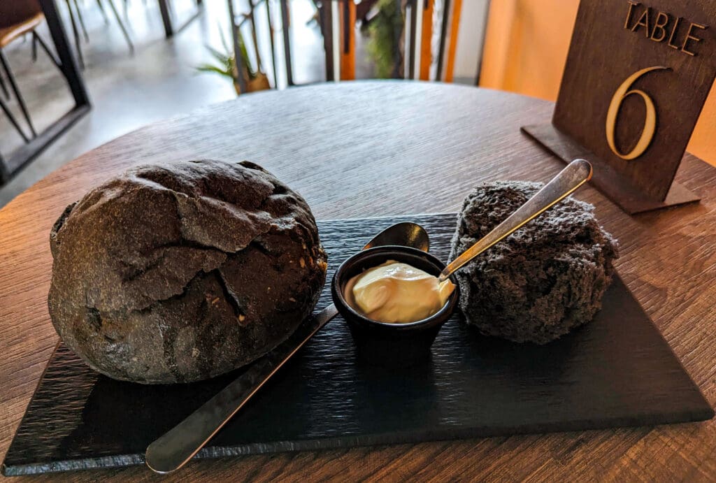 A large black bread bowl with Hot Lava Soup inside along with a fluffy black piece of bread from The Vik Soup Company