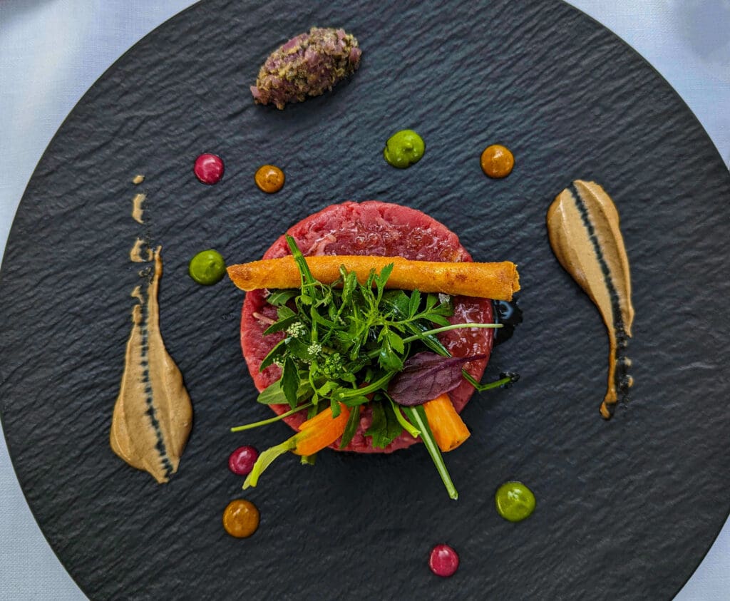 Detailed beef tartare with colorful sauces and garnish decorating the black plate at Villa Margherita restaurant on Capri