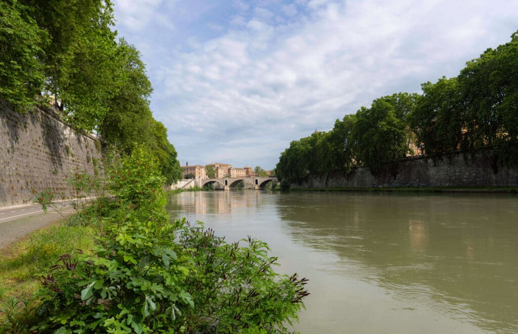 The calm waters run through the center of Rome with trees and a walking path along the sides of the Tiber River 