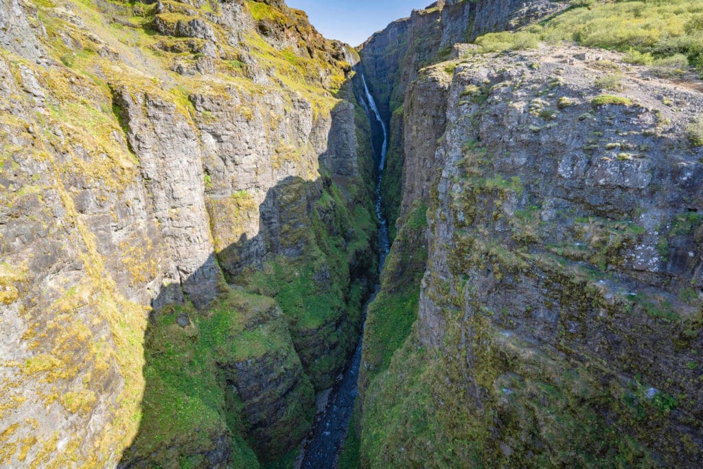 Peering off a cliff down the massive mossy Glymur Canyon as the waterfall plumets in the background