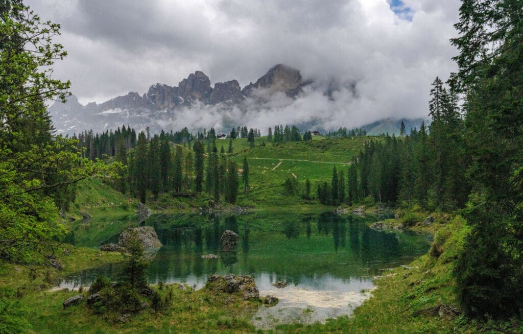 Emerald green waters surrounded by tall trees and mountains in the background at Lake Carezza in the Dolomites