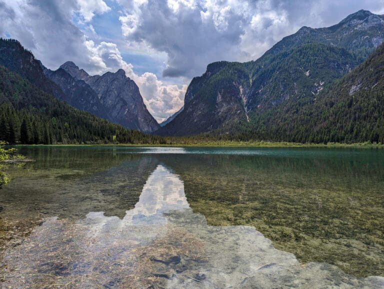 The idyllic still waters of Lake Dobiacco with large mountains in the background is one of the best hikes in the Dolomites