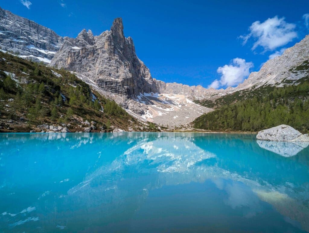 Clear blue sky with forests and dream like blue waters of lake sorapis is the best hike in the dolomites