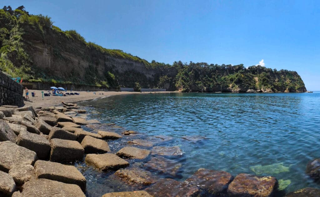 A long sandy italian island beach in front of a curving cliff making creating a cool relaxing bay