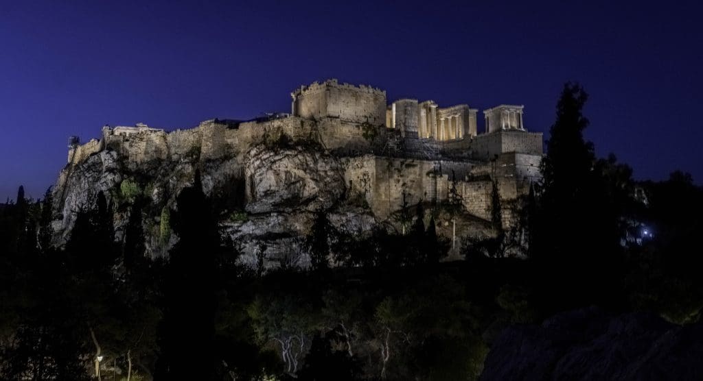 The Athens Acropolis the most famous sight in Greece overlooks the city, fully lit up in front of the night sky.