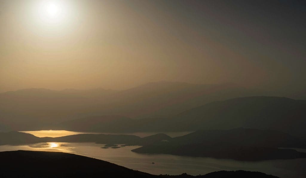 A small boat floats past small Greek islands as the sun rises from Mt. Pantokrator in Corfu.