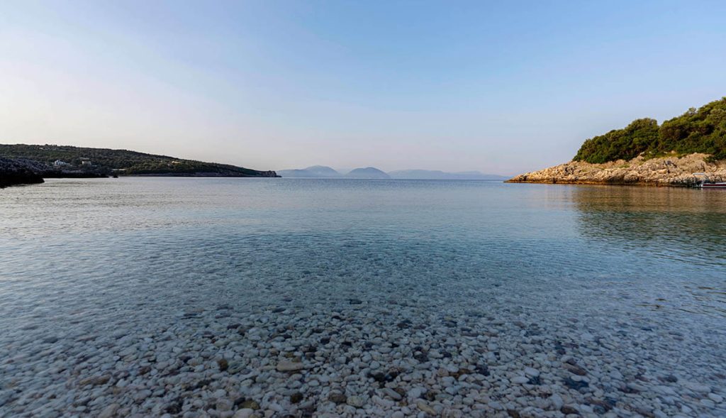 Calm and clear waters sit overtop smooth colored rocks at Ammoussa Beach, one of the best beaches in Greece to relax.