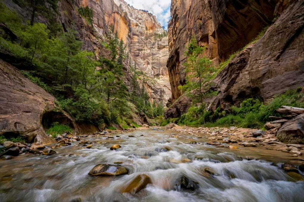 Water rushes over rocks while canyon walls tower above at The Narrows, one of the best photo spots in Zion National Park.