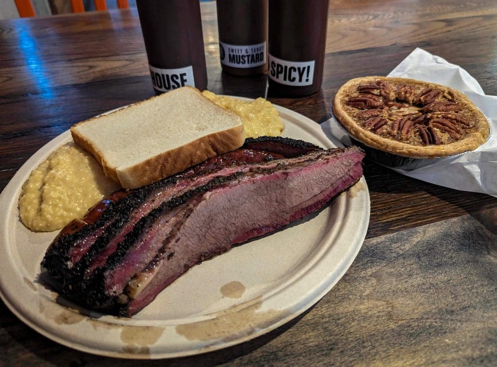 A full plate of tender brisket, warm gritz, bread, and a pecan pie at Little Miss BBQ, one of the best restaurants in Phoenix Arizona.