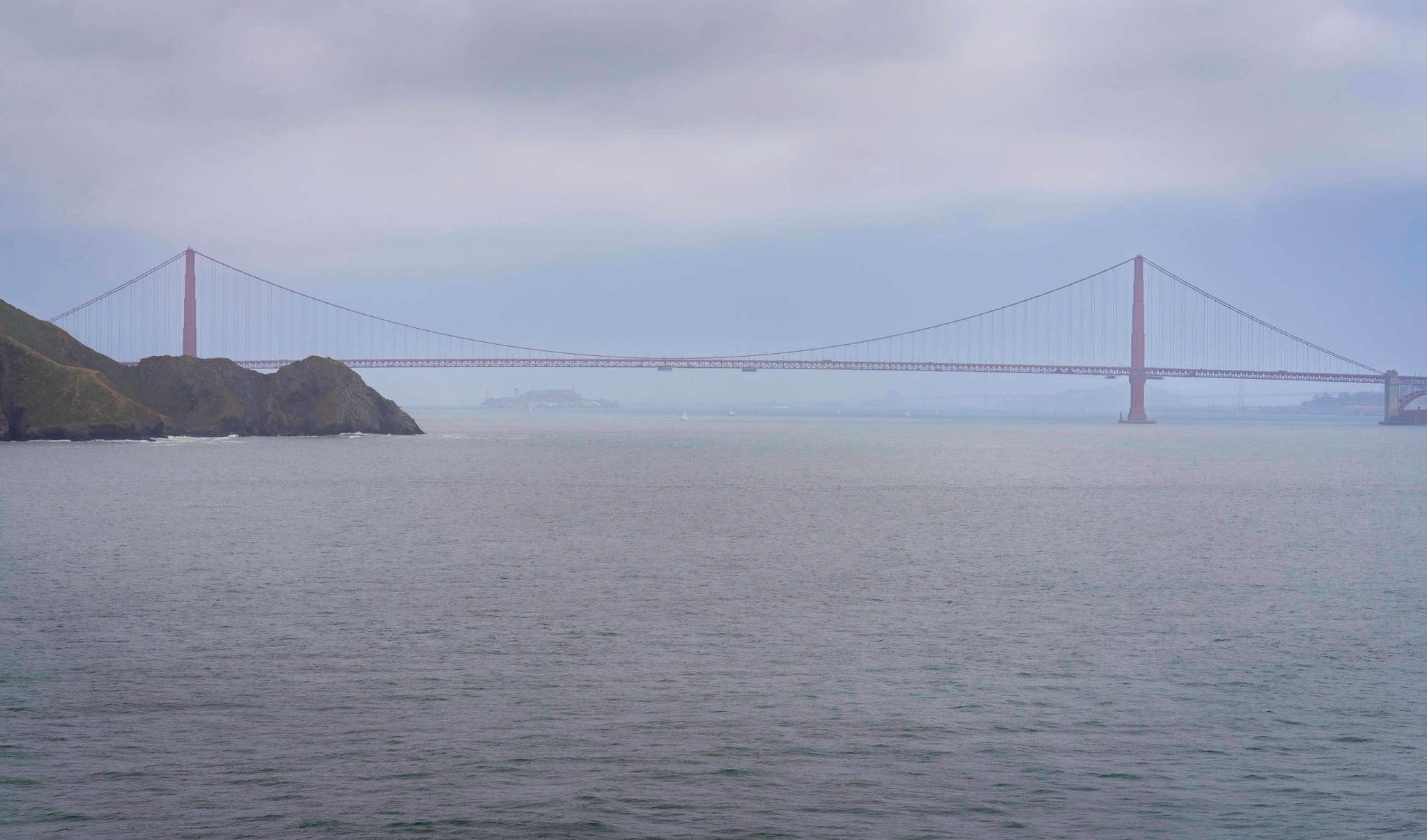 Looking at the distant Golden Gate Bridge from Point Bonita Lighthouse during a peaceful overcast day.