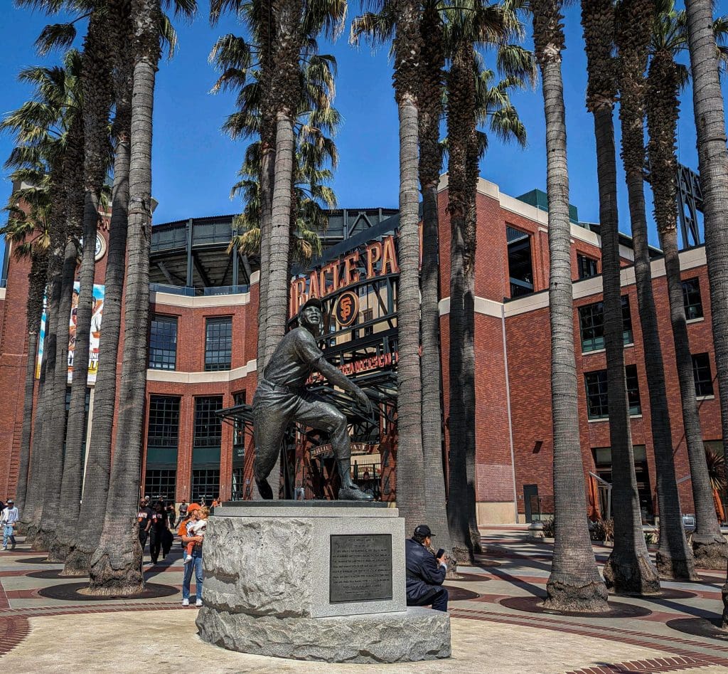 In front of Oracle Park home of the San Francisco Giants with palm trees and a statue of Willie Mayes.