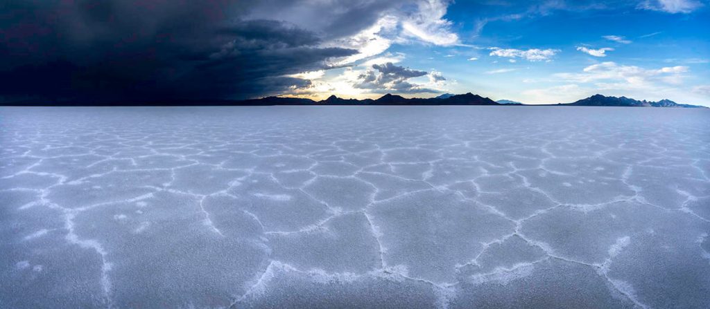 The stark white jigsaw like Utah landscape sits under a sunset sky as a storm rolls in frame.