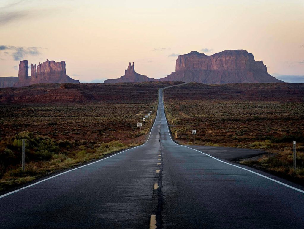 A long and straight road heads down the Utah landscape into the towering formations of Monument Valley.