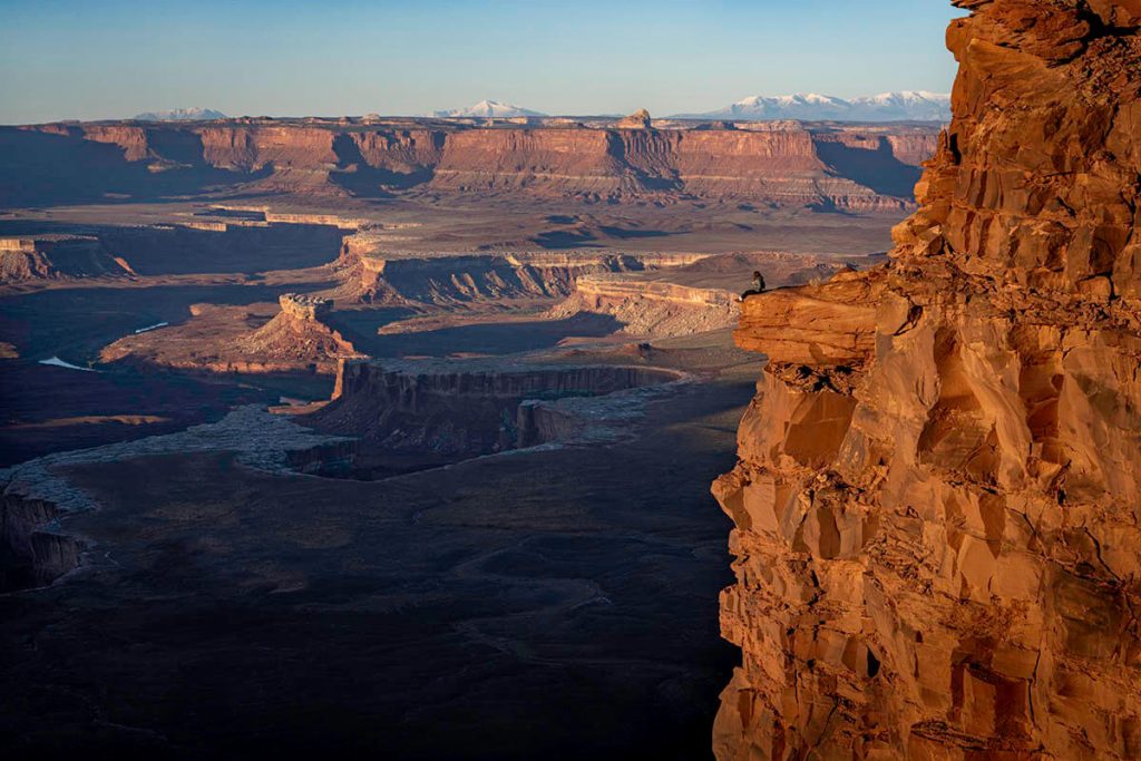 Sitting on the harrowing overlook as the sun rises to illuminate the canyons of the Canyonlands, showing the great Utah outdoor adventures had here.