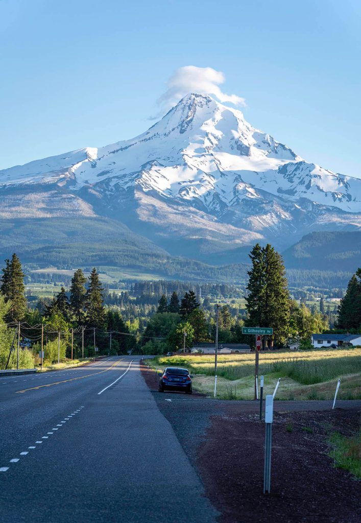 Looking down the road of the open Oregon landscape to see the massive Mt. Hood rising into the sky.