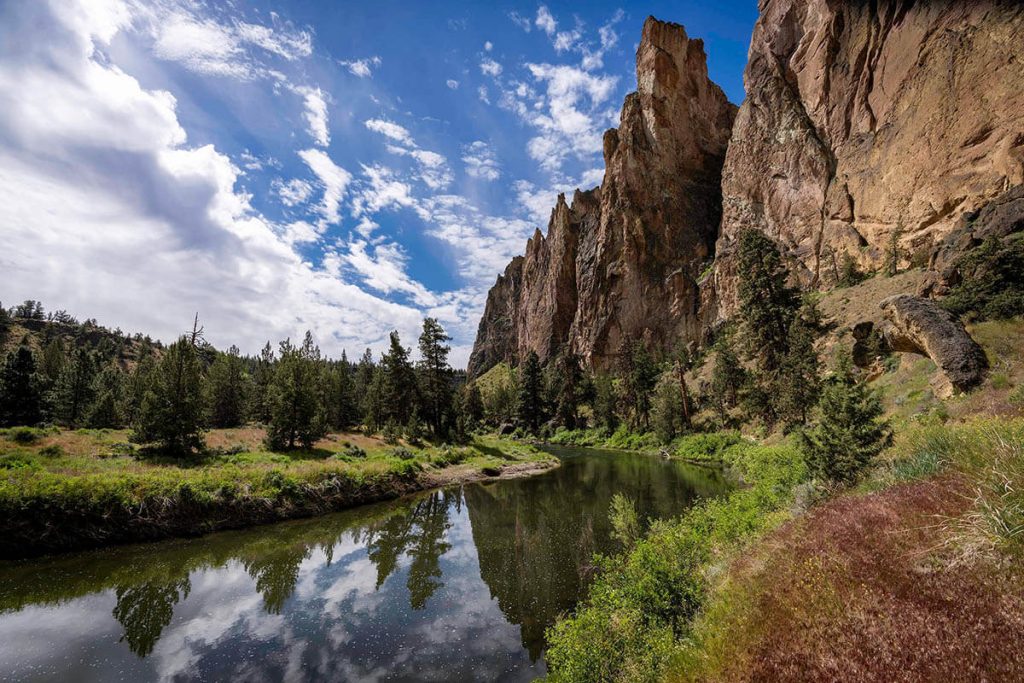 A calm river flows around tall red rocks and lush plant life at one of the best Oregon photography spots.