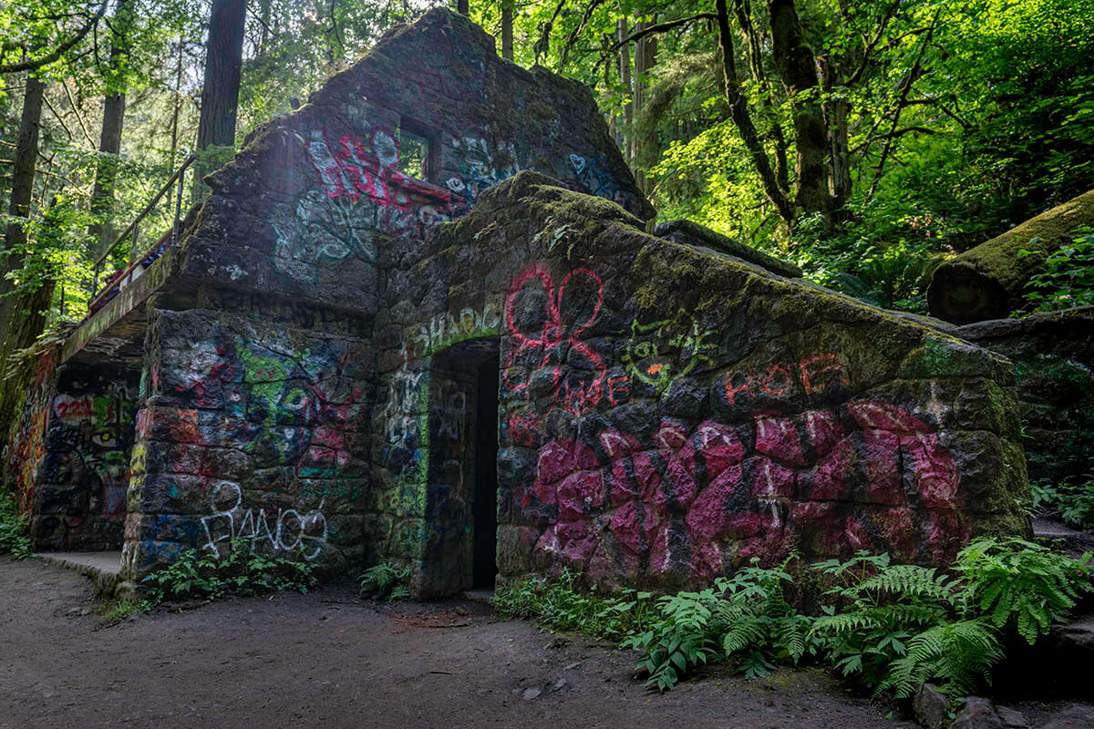 The eerie remains of a stone house sits in the middle of a dense forest in a stunning Oregon landscape.