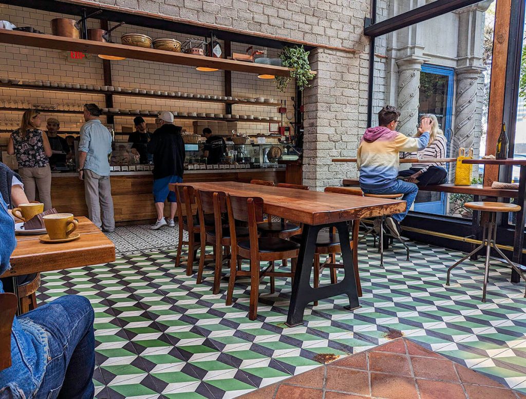 A large dessert display sits behind the open tables and chairs of the beautiful building of Republique Cafe and Bakery.