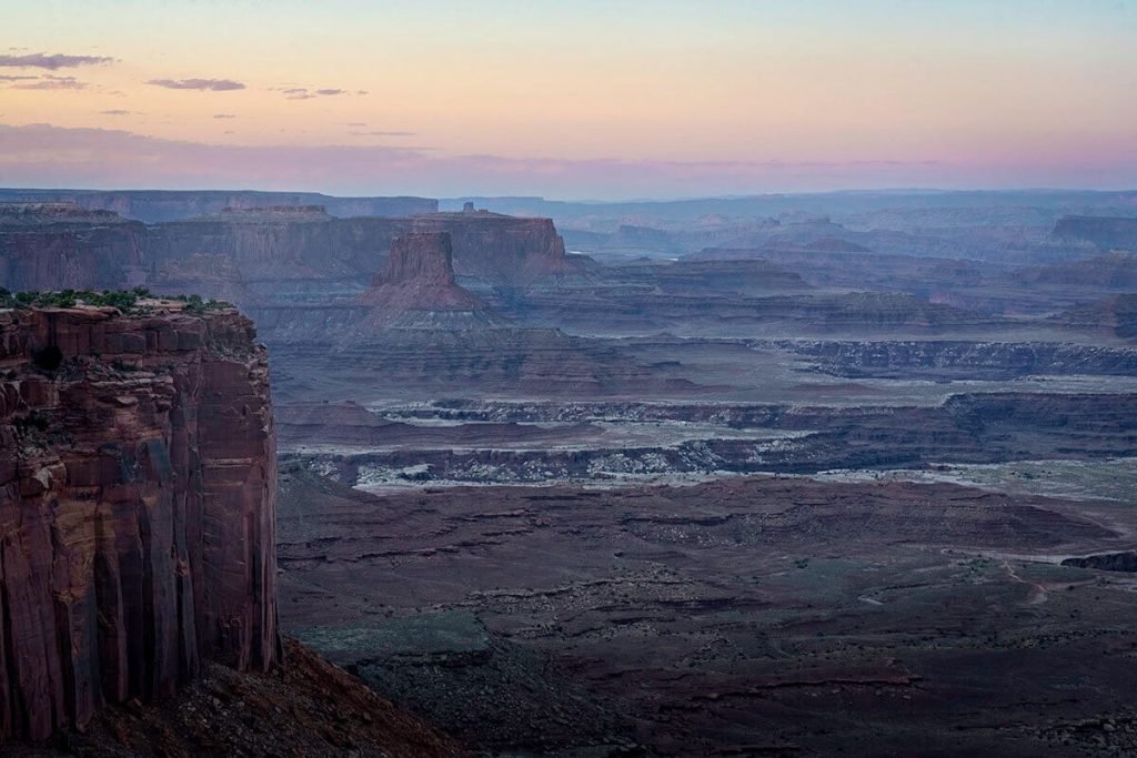 Warm colors of the setting sun wash over the sky above the cliffs and canyons within the Canyonlands from the Grand View Overlook.