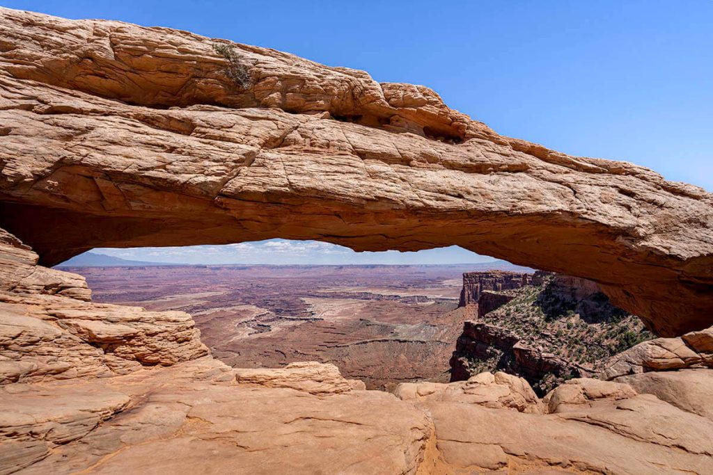 Looking through the low natural arch of the Mesa Arch to the open Canyonlands beyond.